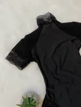 Body de lycra color negro con cuello alto, mangas cortas de microtul y detalles de encaje en el cuello, mangas y laterales. Presenta un diseño entallado con espalda descubierta.
