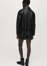 Falda pantalón corta de efecto piel color negro, de tiro medio con diseño cruzado y cierre de cremallera lateral.