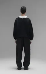 Sweater de punto negro con cuello polo en color crema, manga larga y diseño oversize. Presenta bordados en el frente con la inscripción 'Ravers', el número '90' y letras cursivas, con terminaciones en punto rib en puños y cuello.