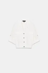 Chaqueta blanca de manga corta con cuello solapa, cierre frontal de botones oscuros y dos bolsillos de plastrón con solapa en el pecho. El bajo es elástico.