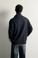 Sudadera negra de corte regular fit, con cuello subido, cierre frontal de cremallera corta y acabados en rib elástico en puños y cintura.