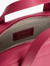Cartera tipo bowling de Tommy Jeans, color fucsia, con doble asa superior y correa ajustable extraíble. Presenta logo metálico de la marca en la parte frontal.