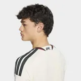Camiseta de fútbol Adidas del Manchester United, correspondiente a la tercera equipación. Es de color blanco marfil con detalles en bordó y negro en el cuello, puños y hombros. Cuenta con el logotipo de Adidas, el escudo del club y un gráfico alineados verticalmente en el centro del pecho.