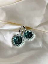 Aros colgantes con forma circular, hechos de resina color lila y borde de strass plateado. El aro es de acero quirúrgico plateado.
