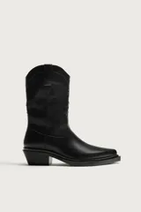 Bota estilo cowboy de color negro, con acabado liso, tiradores laterales, horma en punta, suela a tono y tacón ancho.