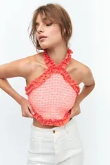 Top de escote halter confeccionado en broderie de algodón y bordado con hilo color coral. Enmarcado con voladitos de lino a tono.