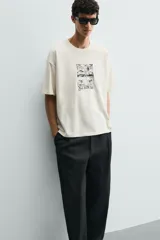 Camiseta de corte relajado color crudo, con cuello redondo y manga corta. Presenta un estampado gráfico en el frente con motivos de palmeras y paisajes en color negro.