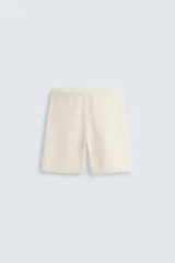 Bermuda de algodón color beige claro, de corte regular fit, con cintura elástica ajustable mediante cordón. Presenta bolsillos laterales y un bolsillo trasero de vivo.