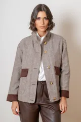 Campera de paño con diseño de espiga en tonos beige y marrón, corte oversize, cuello alto y cierre frontal con botones. Presenta detalles en pana marrón en los puños y en las tapas de los bolsillos frontales.