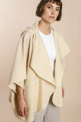 Ruana color crudo de lana fina sin teñir, con capucha, bolsillos y terminaciones envivadas. Tiene un broche para usar cerrada. Es una prenda oversize sin forro, cómoda, versátil y fácil de combinar.