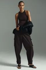 Pantalón cargo de sarga color marrón oscuro, con tiro alto y corte holgado de piernas tipo barrel con pinzas, bolsillos de fuelle con solapa a los lados y trabilla abotonada en el bajo.