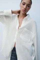 Camisa oversize blanca de cuello solapa y manga larga con puños anchos. Cuenta con cierre frontal de botones y un bolsillo aplicado en el frente.