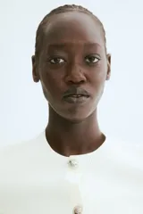 Cárdigan corto color blanco, de punto fino, con cuello redondo, mangas cortas, cierre frontal con botones metálicos decorativos y bolsillos delanteros simulados con botón.