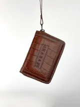 Mini billetera de cuero con textura efecto cocodrilo y cierre perimetral. Presenta un parche central con el logo de la marca grabado.