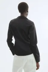 Camisa de manga larga en tejido elástico, con cuello clásico, cierre frontal de botones y puños abotonados. Presenta pinzas delanteras y traseras que definen la silueta y bajo levemente redondeado.