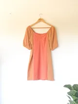 Vestido corto de algodón en calidad tusor con diseño en bloque de color, combinando un panel central coral con laterales y mangas abullonadas en color tostado. Presenta escote cuadrado con frunce en el centro del busto.
