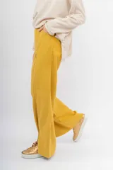 Pantalón ancho de color mostaza con costuras contrastantes en blanco. Presenta un corte recto y aberturas en los bajos delanteros.