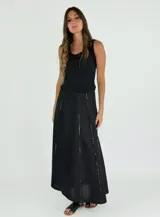 Pollera larga negra de corte amplio, con costuras verticales que simulan pliegues y terminaciones deshilachadas. Se combina con una musculosa negra de escote redondeado.