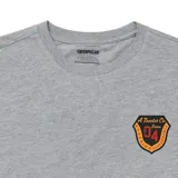 Remera de manga corta color gris melange, con cuello redondo y estampado gráfico tipo escudo en el pecho izquierdo.