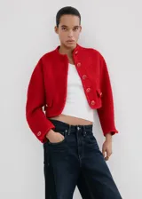 Chaqueta corta roja de tejido texturizado tipo tweed, con cuello redondo, bolsillos frontales con solapa, mangas largas y cierre de botonadura frontal con botones decorativos.
