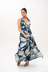 Vestido largo con escote halter profundo y diseño sin mangas. Presenta un estampado difuminado en tonos azules, celestes, blancos y grises, con corte ajustado en el torso y una falda larga con vuelo.