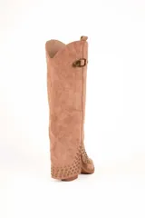 Bota de caña alta estilo slouchy confeccionada en gamuza sintética de color negro, con punta fina y taco bajo. Presenta solapa superior plegada con apliques de tachas metálicas plateadas y una tira con hebilla decorativa en la parte superior de la caña.