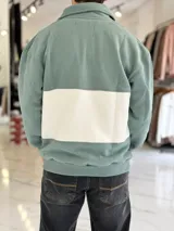 Buzo de algodón negro con una franja horizontal blanca en el centro, cuello solapa con medio cierre y puños y cintura elásticos acanalados. Cuenta con pequeños estampados en el pecho.