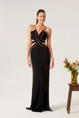Vestido largo de fiesta negro con breteles finos, escote en V, aberturas laterales en la cintura y tajo en la falda. Decorado con una cadena dorada que cruza el torso y continúa como collar.