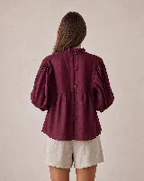 Blusa holgada color blanco, de manga por debajo del codo con elástico y volados en los puños. Presenta cuello alto con volados y diseño fruncido tipo nido de abeja hecho a mano en la parte superior delantera.