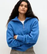 Suéter de punto azul con cuello alto y cierre frontal de cremallera metálica. Presenta textura de líneas verticales, corte regular, mangas largas y terminaciones acanaladas.