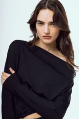 Top negro de manga larga, con escote asimétrico estilo off-shoulder y diseño drapeado.