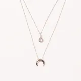 Colgante doble de acero plateado. La cadena superior tiene un dije de cristal redondo y la inferior un dije en forma de media luna.