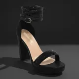 Sandalia de fiesta con plataforma y taco cuadrado alto, confeccionada en material brillante color negro. Presenta una tira frontal ancha y una correa ajustable al tobillo con hebilla metálica.