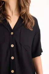 Camisa de lino color beige, de manga corta, con cuello camisero, bolsillos delanteros con solapa y cierre frontal con botones de madera.