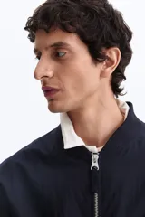 Campera bomber en mezcla de algodón y nylon color azul marino, con cuello elevado acanalado, cierre frontal, bolsillos laterales y un bolsillo con cierre en la manga.