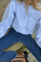 Camisa de manga larga con estampado de cuadros vichy en tonos celestes y blancos. Presenta un diseño con pliegues verticales en el frente, cuello redondo y cierre frontal con botones.
