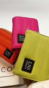 Billetera corta de diseño capitoneado con cierre perimetral y solapa frontal. Cuenta con compartimentos internos para tarjetas y billetes, e incluye una correa de mano desmontable.