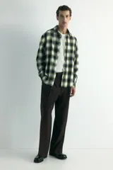 Camisa de franela de algodón suave con cuello inglés, cierre frontal de botones, mangas largas con puños abotonados y bajo redondeado. Presenta un diseño a cuadros en tonos oscuros y amarillentos.