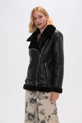 Chaqueta negra de cuero sintético con interior de piel sintética, corte al cuerpo, cierre frontal asimétrico con cremallera, cuello solapa con hebillas y cinturón con hebilla en la cintura.