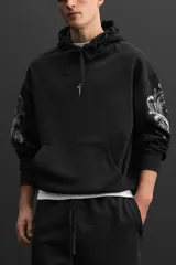 Hoodie negro oversize con estampado de cruz en el pecho y diseño floral en las mangas.