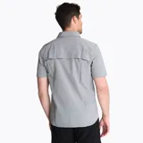 Camisa de manga corta Merrell, color gris cemento, con cuello clásico, cierre frontal de botones y dos bolsillos frontales con solapa en el pecho. Presenta un diseño funcional con tejido técnico transpirable.
