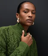 Suéter de punto color verde oliva con diseño de trenzas, cuello alto y mangas largas. Presenta un corte corto con terminaciones acanaladas en puños, cuello y ruedo.