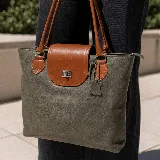 Cartera tote de cuero vacuno color marrón con solapa negra y cierre metálico. Tiene doble asa de mano negra, bolsillo interno con cierre y cierres YKK metálicos.