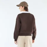 Buzo de felpa color marrón con cuello polo blanco en contraste. Presenta un estampado gráfico frontal con estilo universitario que incluye la inscripción 'Wellington Florida' y un emblema central.