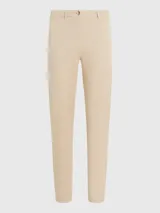 Pantalón chino color beige de sarga elástica, corte slim, con cierre de cremallera y botón, bolsillos traseros de ojal y logo de Tommy Hilfiger bordado en la parte trasera.