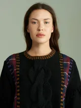 Sweater oversize de lana color negro con diseño de trenza central, paneles laterales en tela escocesa (cuadrillé) y detalles de pespuntes contrastantes. Presenta cuello redondo, mangas acampanadas con terminaciones desflecadas y aberturas laterales con cordones ajustables.