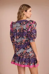 Blusa de algodón con estampado floral en tonos azul, rosa y naranja. Tiene cuello redondo con lazo y mangas cortas abullonadas con volados rosas.