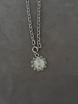 Collar de cadena gruesa de eslabones con dije circular con relieve de la Virgen de Guadalupe rodeada de rosas, fabricado en metal plateado.
