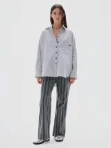 Camisa oversized de algodón color gris claro, con cuello clásico, botones negros y bolsillo frontal con etiqueta de marca.