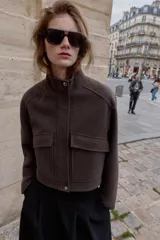 Cazadora de corte corto y diseño estructurado, confeccionada en tejido de paño color marrón. Presenta cuello subido, manga larga, bolsillos delanteros de plastrón con solapa y cierre frontal con cremallera oculta y botones a presión.